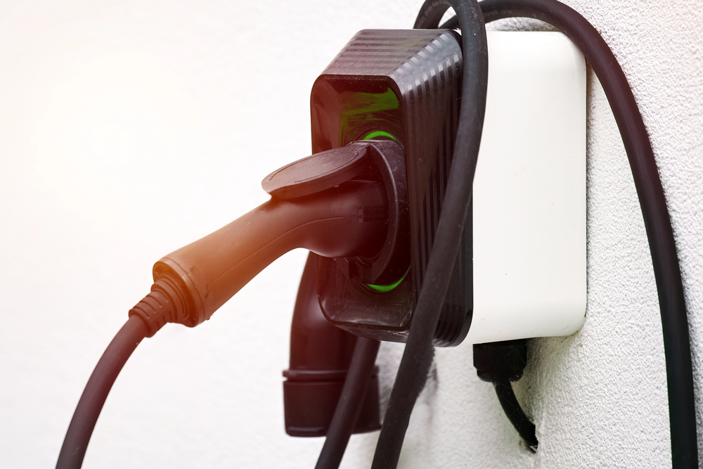 Close-up of a black electric car charging plug connected to a wall-mounted charging station, highlighting the cables and tidy EV charger installation.