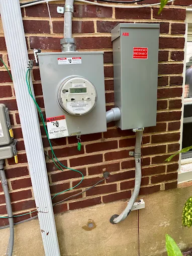 An electric meter and an emergency disconnect switch mounted on a brick wall, with wires and conduits connected.